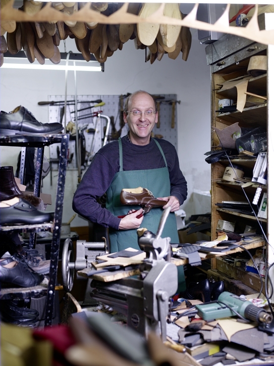 Axel Gemmel mit grüner Schürze und einem Schuh in seiner Werkstatt